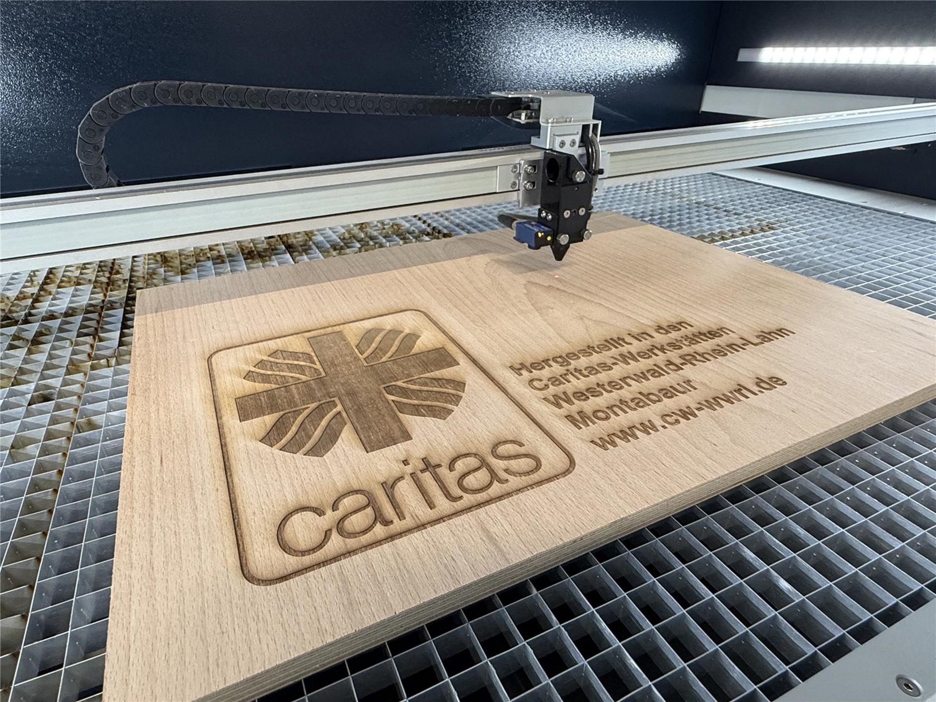 Der Laser graviert das Caritas-Logo in ein Holzbrett.
