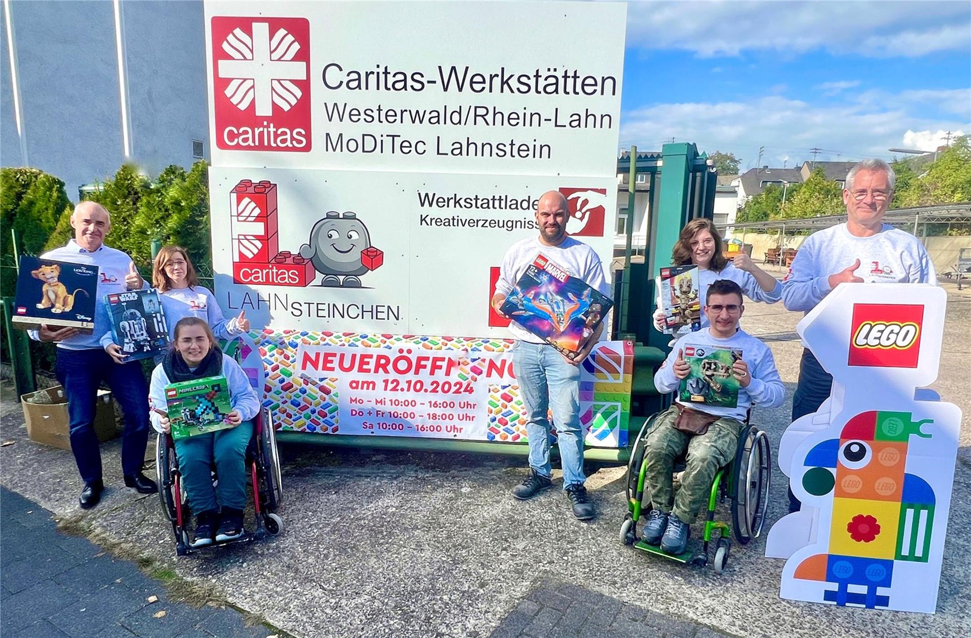 Die Beschäftigten und Mitarbeitenden des MoDiTec-Betriebes stehen vor dem Eingang mit dem großen Schild, dass auf die Neueröffnung des LEGO-Ladens hinweist.
